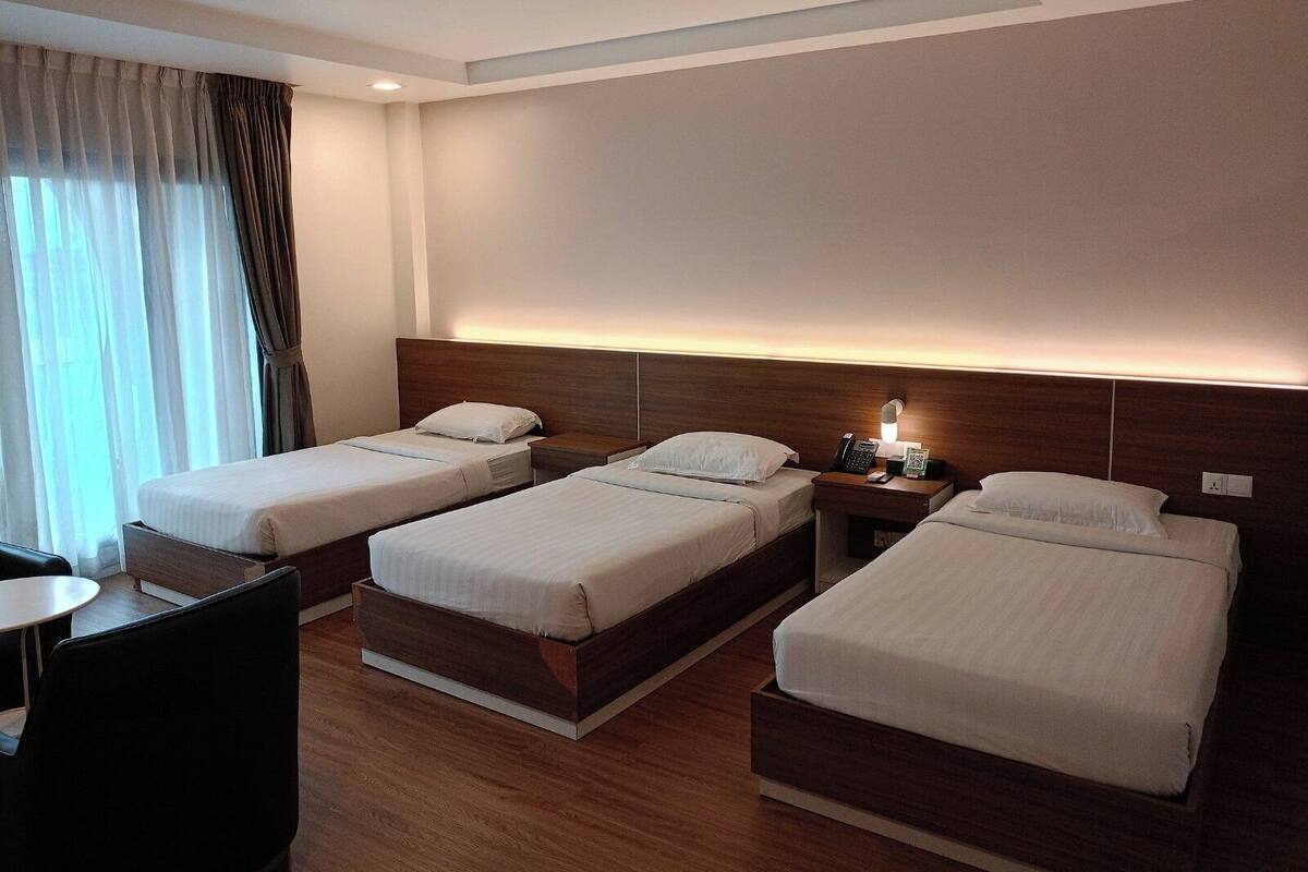 Una habitación de hotel con tres camas individuales, un escritorio y una silla.