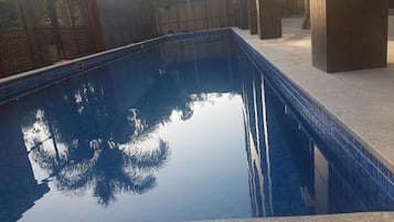A rectangular pool with clear water reflecting trees and a fence.