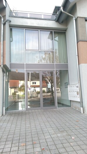 A building with a glass entrance, metal railings, and a tiled ground.
