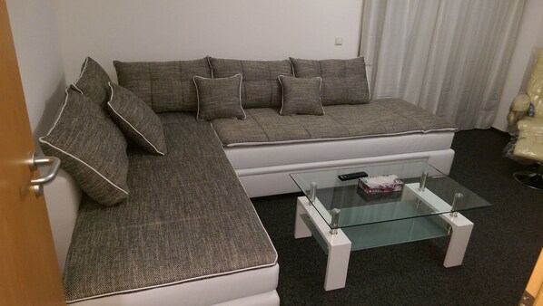 A modern living room with a grey sectional sofa, a glass coffee table, and a white armchair.