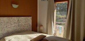 Ein Schlafzimmer mit einem Kopfteil aus runden Objekten, einer Nachttischlampe und Blick auf einen Balkon mit Wäsche zum Trocknen.