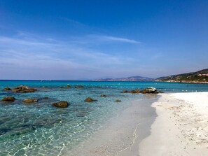 Una playa con agua cristalina, rocas y una orilla arenosa.