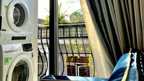 Ein Waschbereich mit einer Waschmaschine und einem Trockner mit Frontlader, einem Fenster mit Vorhängen und Blick auf den Balkon mit Pflanzen.