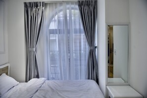 Una habitación de hotel con cama, mesita de noche, espejo y ventana con cortinas.