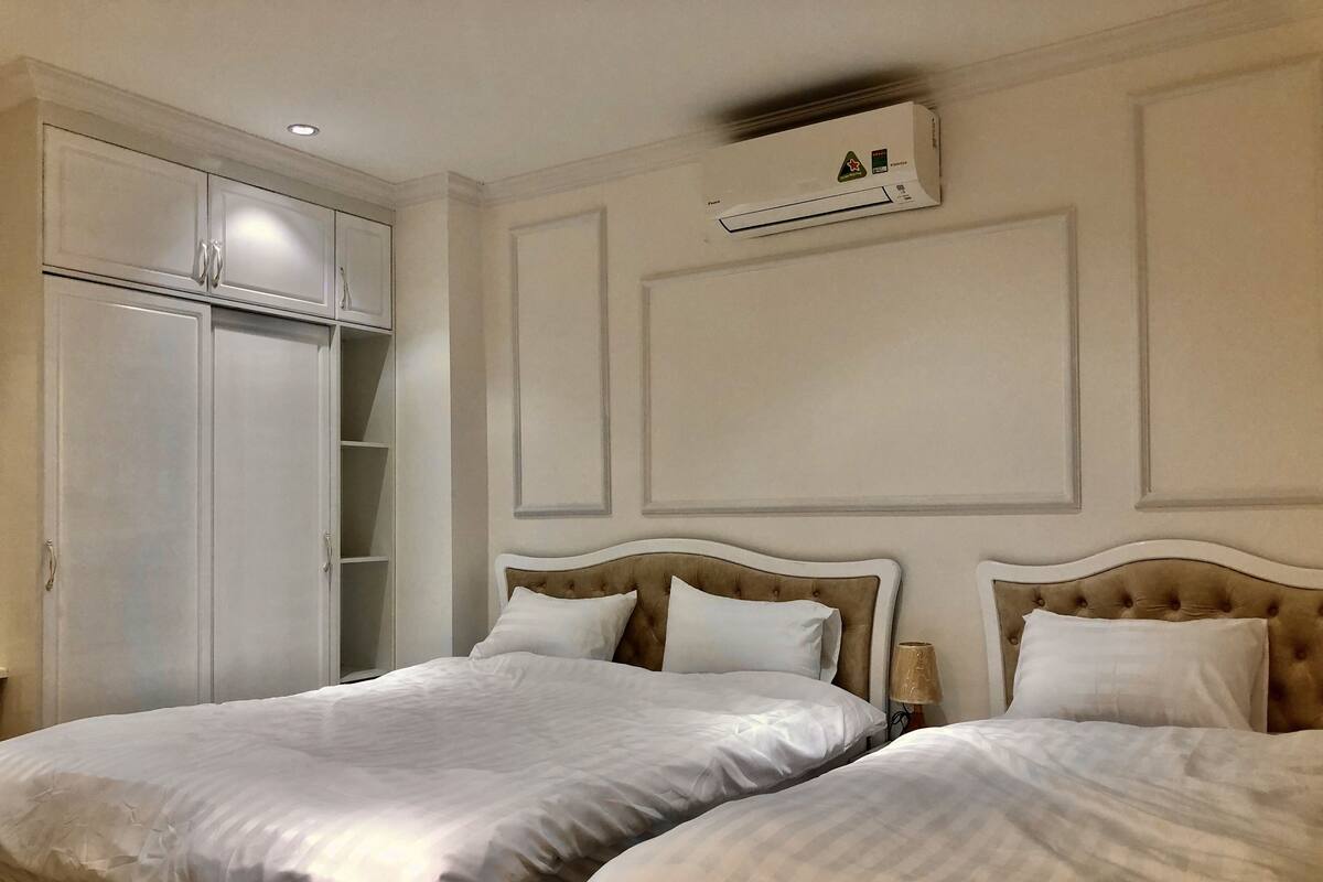 A hotel room with two beds, a wardrobe, and an air conditioning unit.