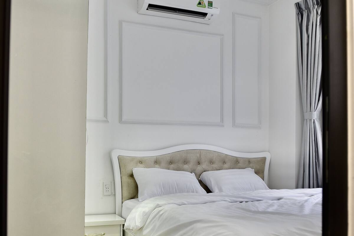 A neatly arranged bedroom with a bed, bedside table, and an air conditioning unit mounted on the wall.