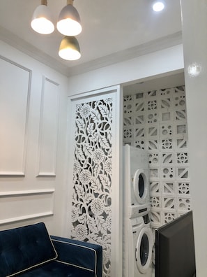 Una habitación con un sofá azul, un panel decorativo blanco y una lavadora.