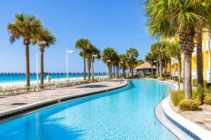 A swimming pool with a curved edge, surrounded by palm trees and a beach view.