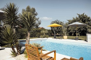 Una piscina con sillas de descanso y sombrillas, rodeada de palmeras y un jardín.
