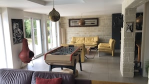 Ein Wohnzimmer mit einer Tischfußballplatte, einem Sofa, einem gelben Sessel und einer roten Vase.