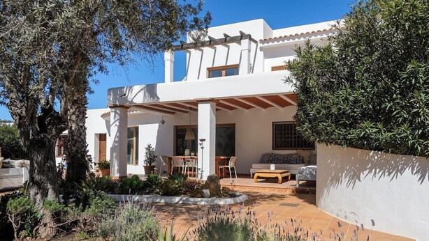 A modern house with a patio area, outdoor seating, and a garden with various plants.