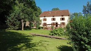 A two-story building with a tiled roof, surrounded by lush greenery and a well-maintained lawn. - La Charmante (Xertigny)