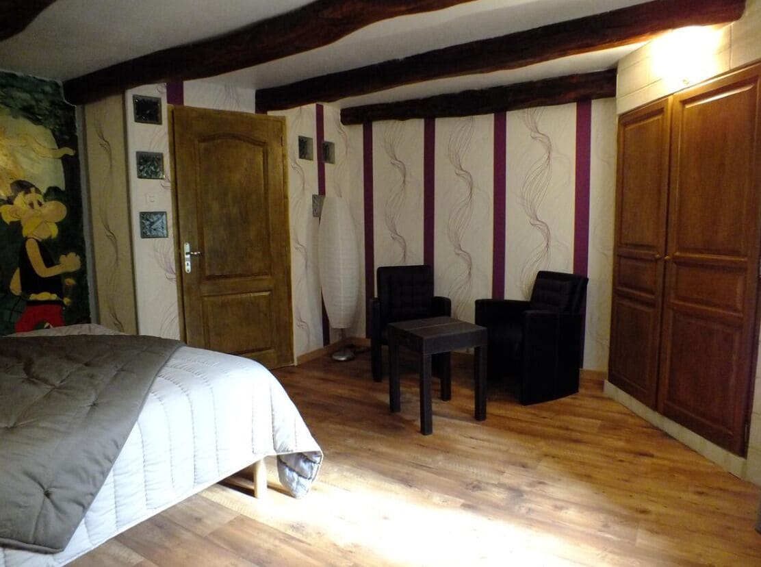 A room with a bed, two chairs, a wooden door, and a wardrobe.