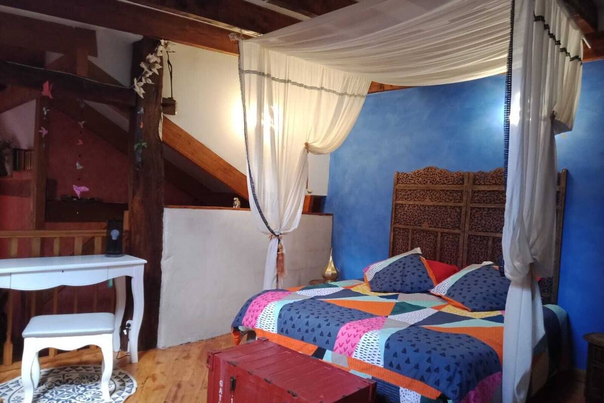 A bedroom with a bed, a small table, a bench, a decorative headboard, and a curtain.