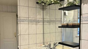 A bathroom with a marble sink, black cabinetry, and a mirror with shelves. - La Charmante (Xertigny)