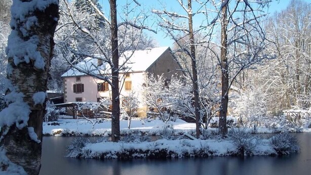 A house with a sloped roof, surrounded by snow-covered trees and a small body of water. - La Charmante (Xertigny)