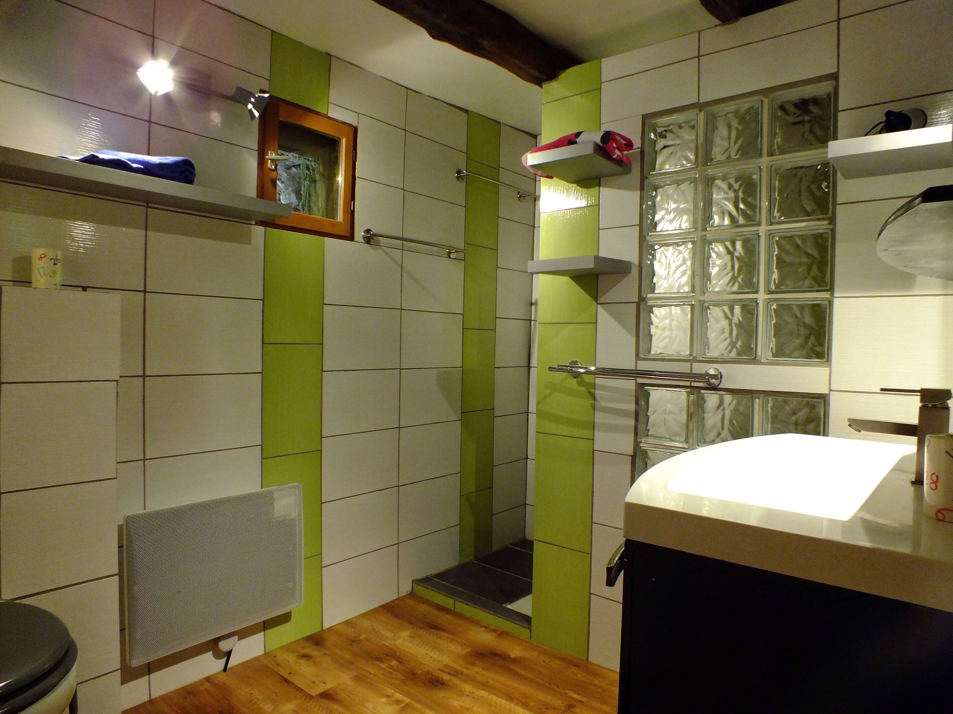 Un baño con piso de madera, un lavamanos blanco, un espejo y zona de ducha.