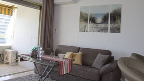 En stue med en brun sofa, et glasbord og et billede med strandmotiv.