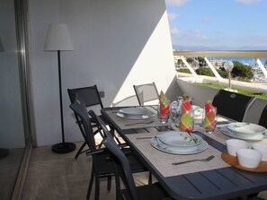 Un espace de restauration en plein air avec une table dressée pour quatre personnes, des chaises, une lampe et une vue sur la mer.