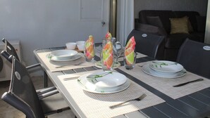 Et udendørs spiseområde med et bord dækket til to, inklusiv tallerkener, bestik og drikkeglas.