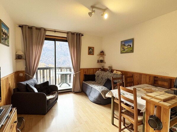 A cozy living room with a sofa, a dining table, and a view of a mountainous landscape through a large window.