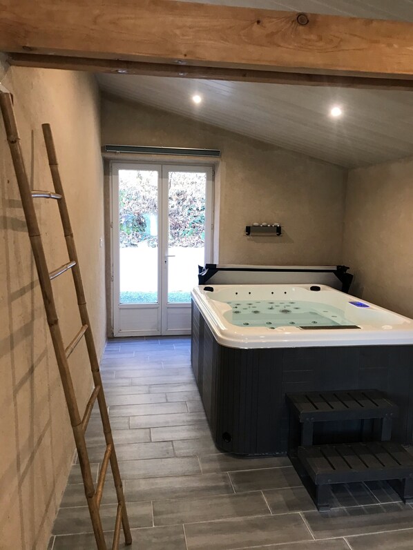 A spa room with a hot tub, wooden flooring, and a ladder.
