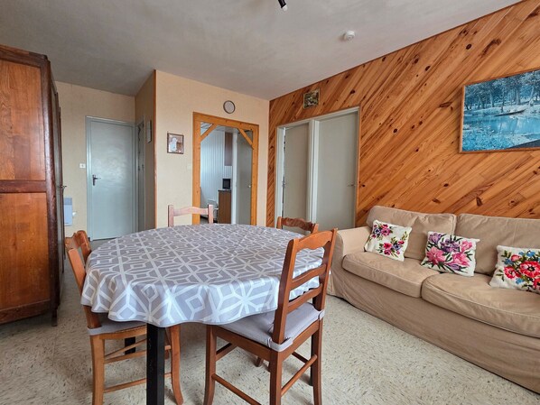 A room with a dining table, chairs, a sofa, and a painting on the wall.