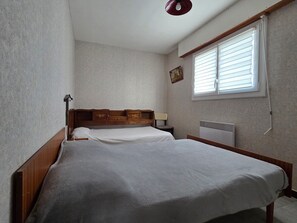 A bedroom with two beds, a radiator, a window with blinds, and a picture on the wall.