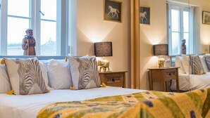 Een slaapkamer met een bed, kussens, een nachtkastje, een lamp en een spiegel.