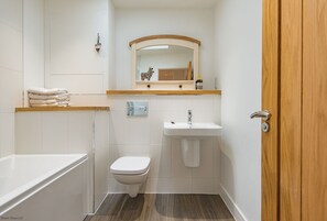 Een badkamer met een bad, toilet, wastafel en een spiegel boven de wastafel.