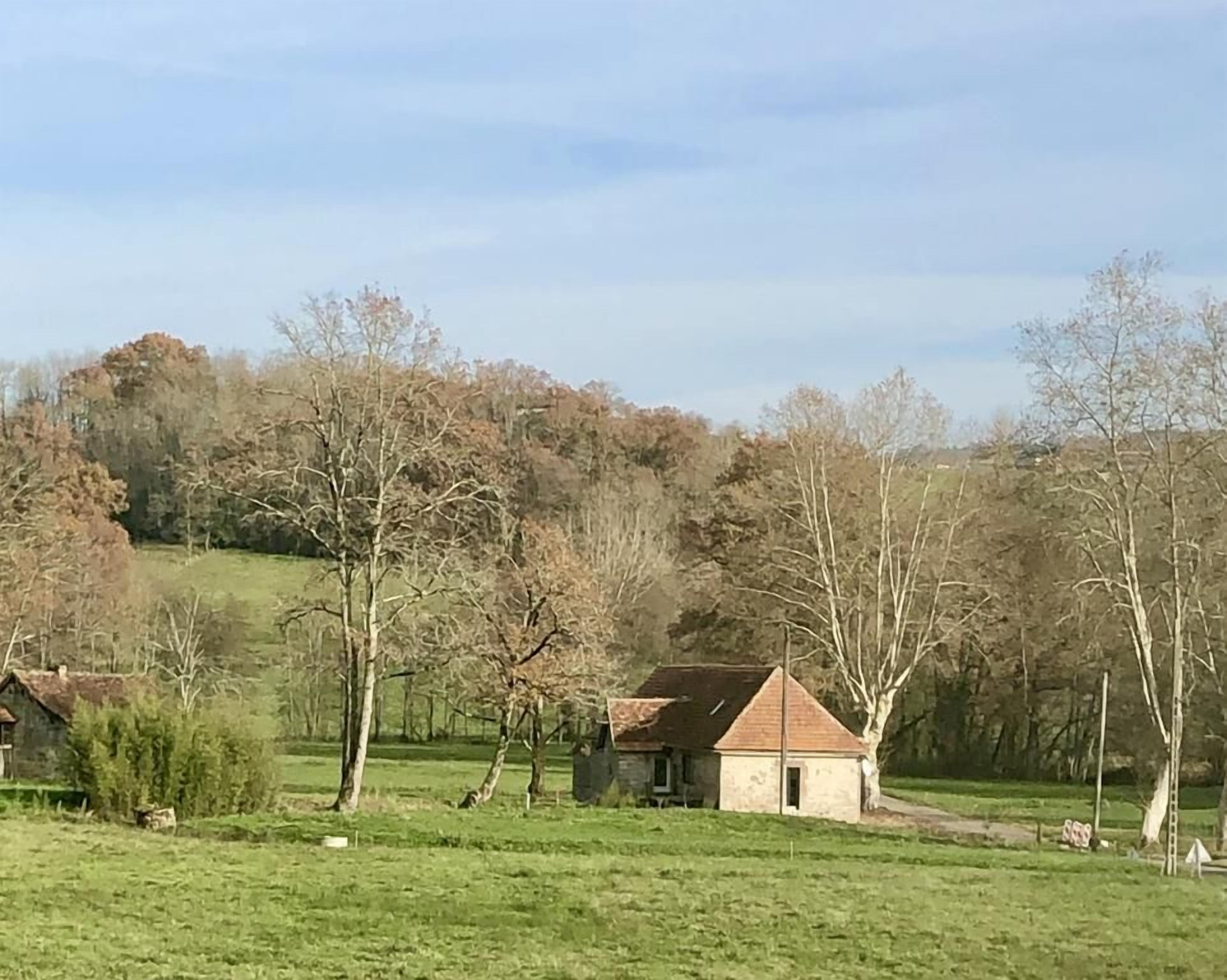 Paisaje rural con una casa pequeña rodeada de árboles y campos abiertos.