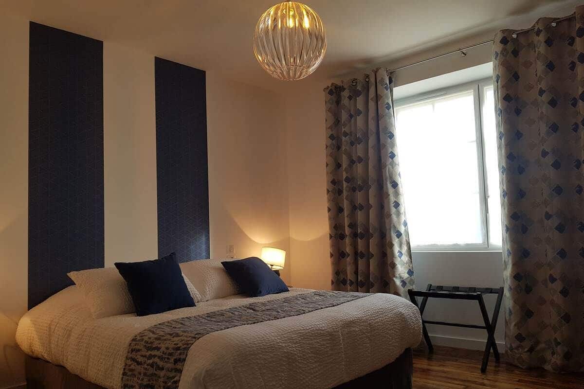 Une chambre à coucher avec un grand lit, une table de chevet, une lampe et une fenêtre avec des rideaux.