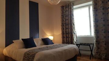 Een slaapkamer met een groot bed, een nachtkastje, een lamp en een raam met gordijnen.