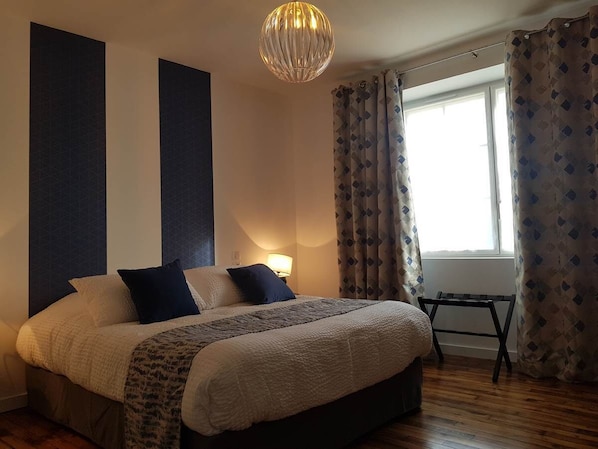 Un dormitorio con una cama grande, una mesita de noche, una lámpara y una ventana con cortinas.