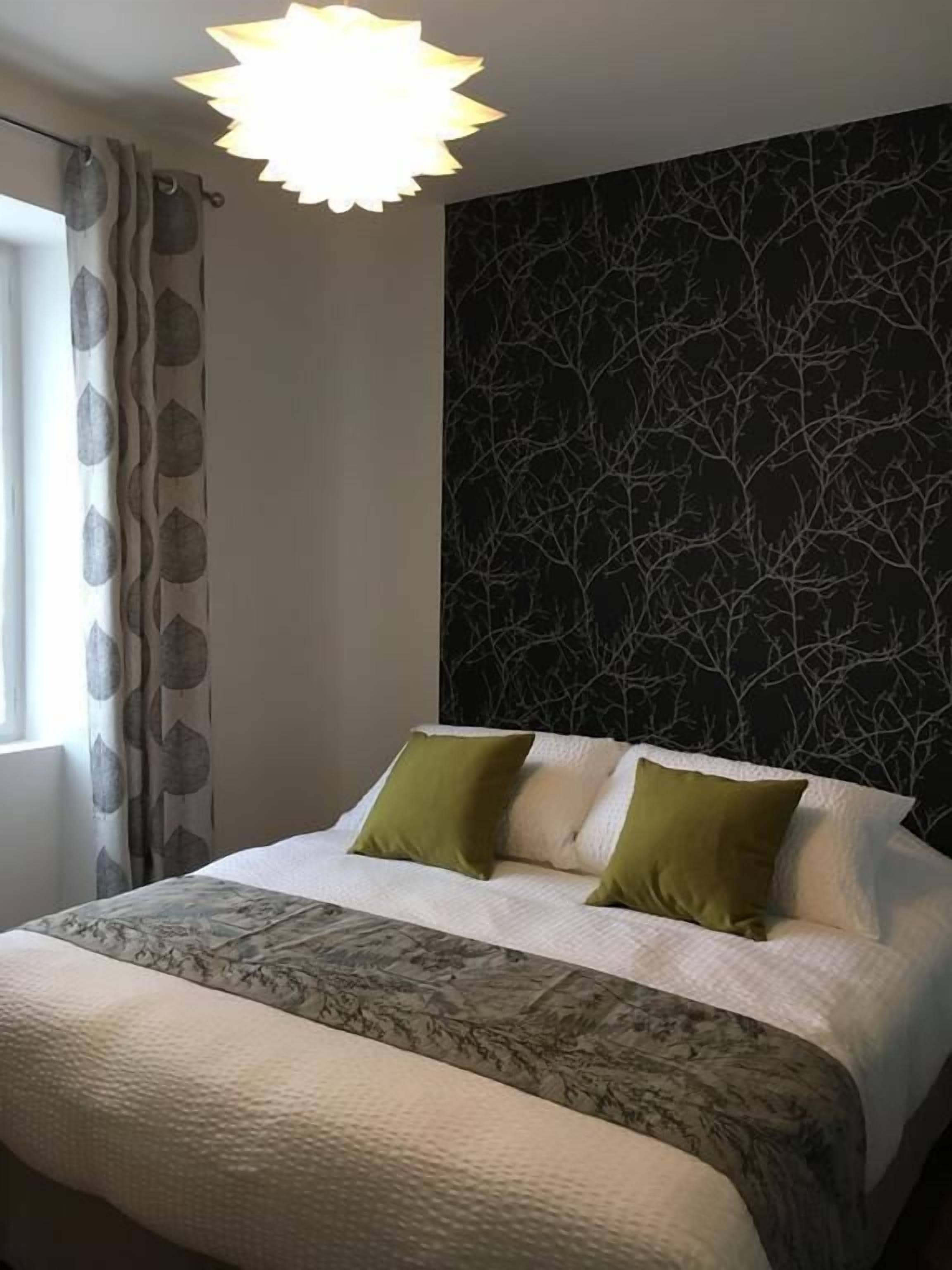 A bedroom with a bed, a patterned headboard, and a window with curtains.