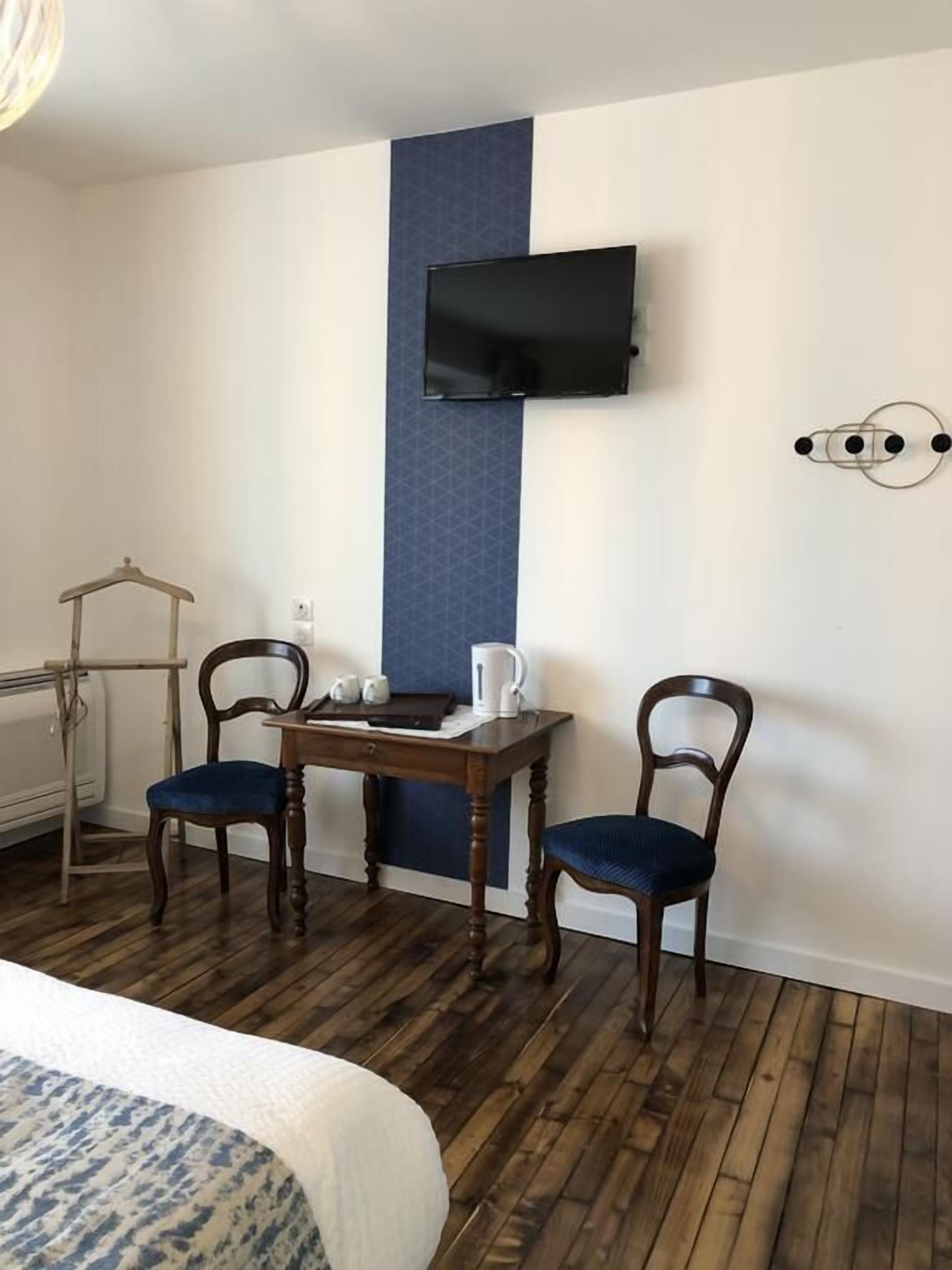 Habitación de hotel con cama, una mesa de madera con dos sillas, un televisor montado en la pared y un radiador.