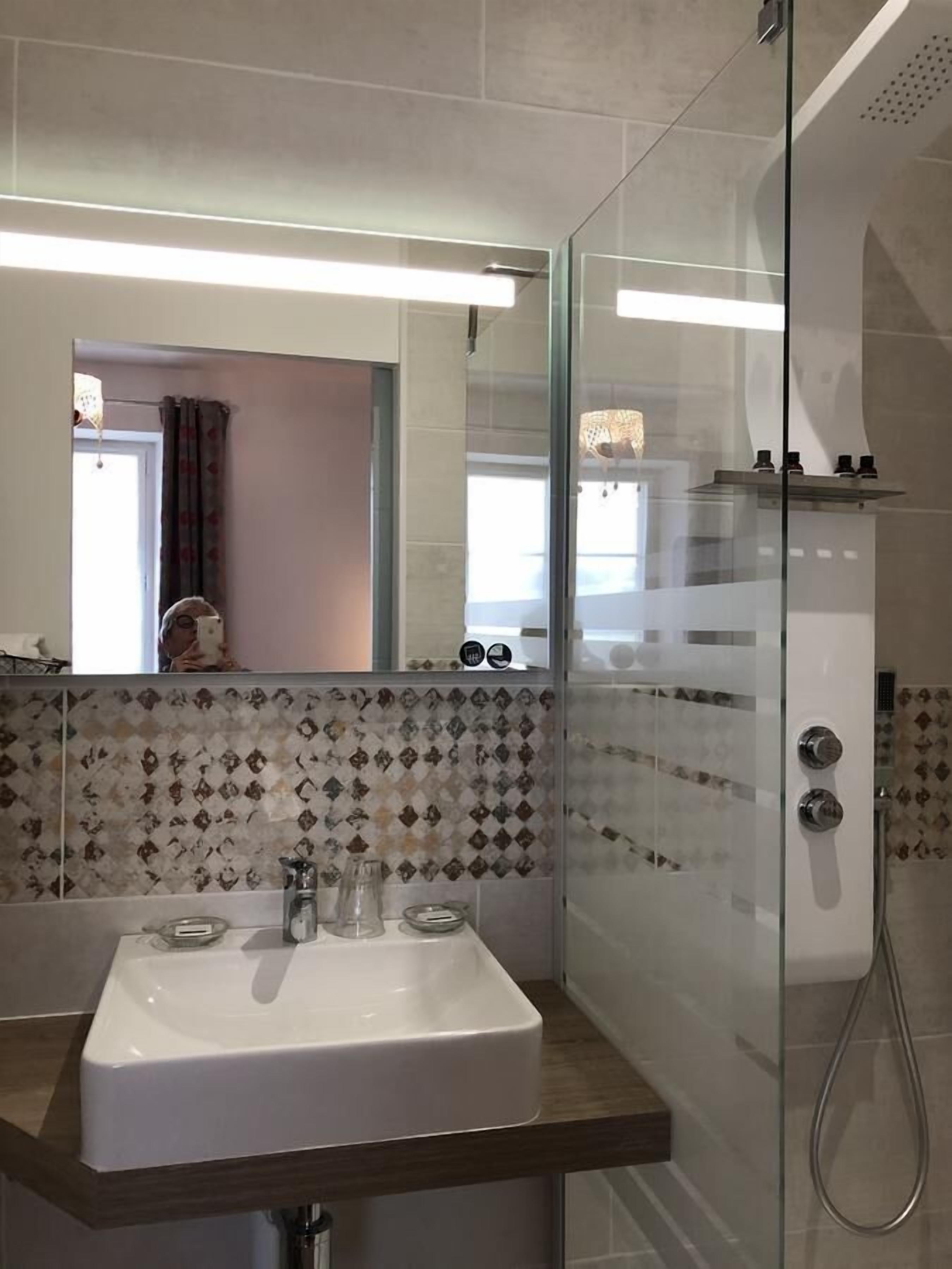 A modern bathroom with a glass shower enclosure, a white sink with a wooden countertop, and a tiled backsplash.
