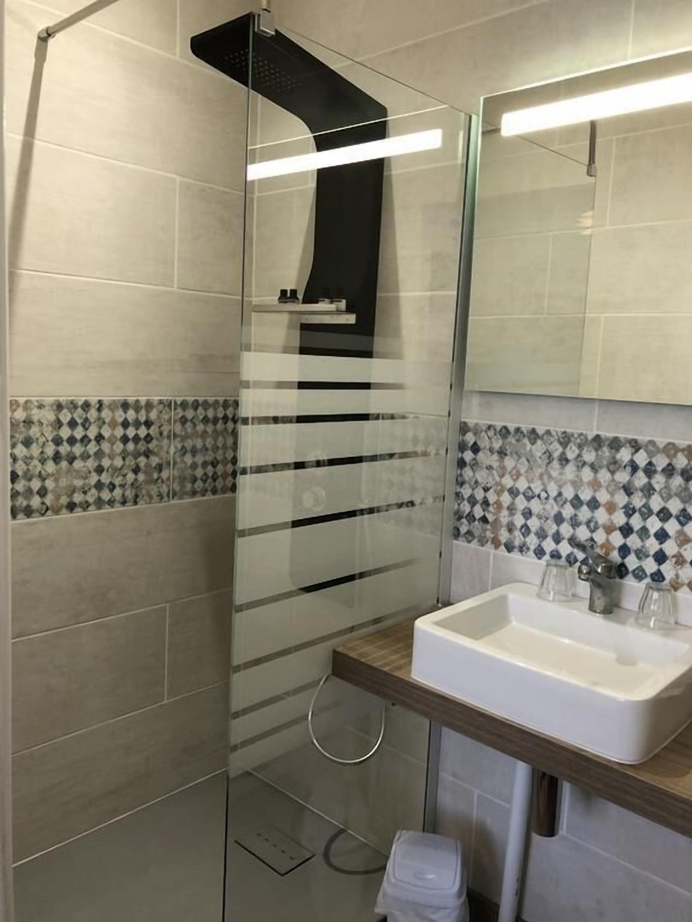 Un baño moderno con cabina de ducha de vidrio, un lavamanos blanco con encimera de madera y un salpicadero de azulejos con diseño de diamantes.