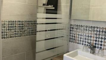 Un baño moderno con cabina de ducha de vidrio, un lavamanos blanco con encimera de madera y un salpicadero de azulejos con diseño de diamantes.