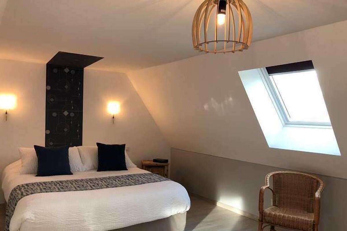 Une chambre à coucher comprenant un lit, une chaise, un puits de lumière et un luminaire fixé au mur.