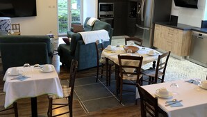 Een eetruimte met tafels voor vier personen, een bank en een keuken op de achtergrond.