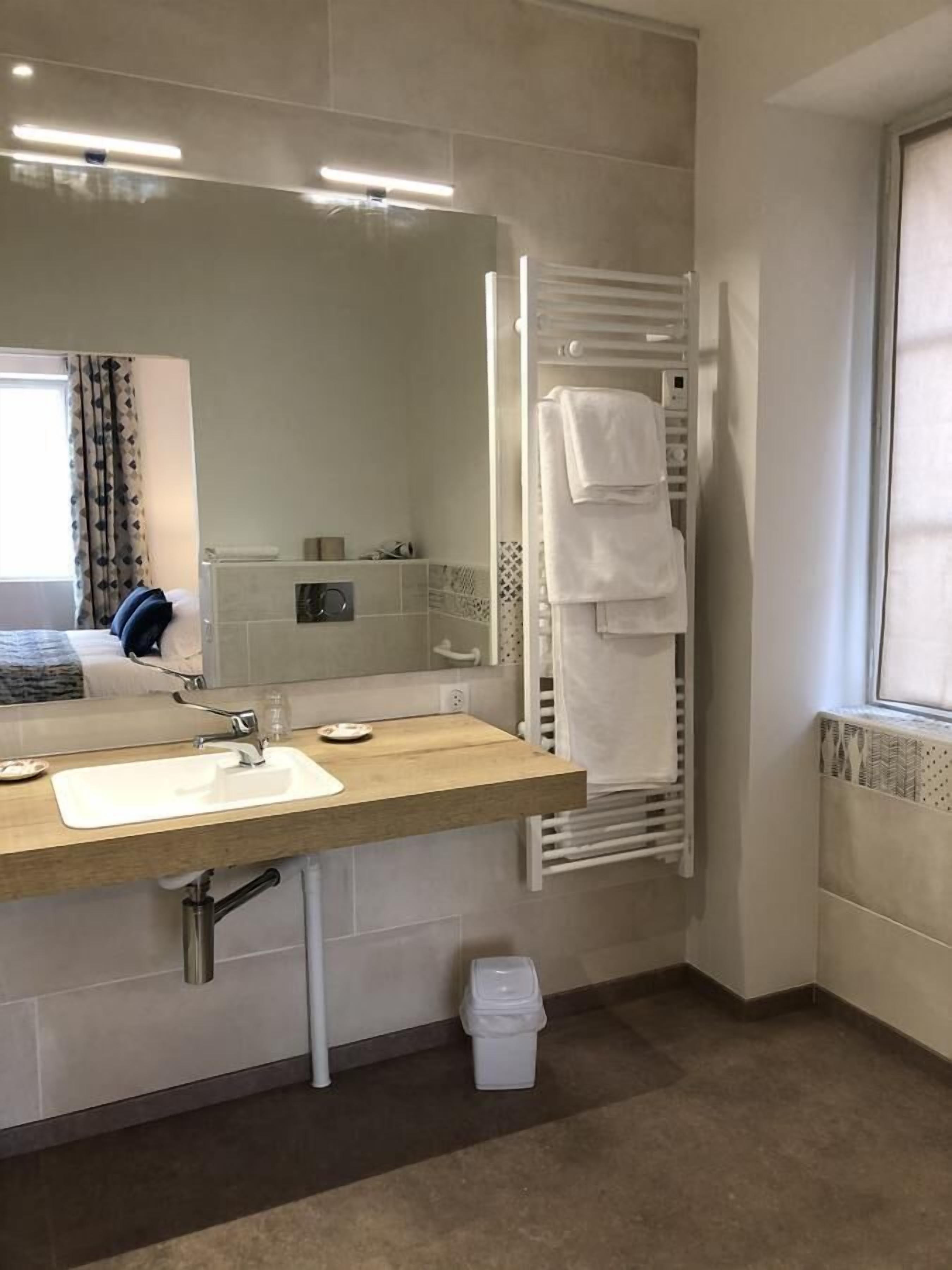 A modern bathroom with a wooden vanity, a large mirror, a towel rack, and a window.