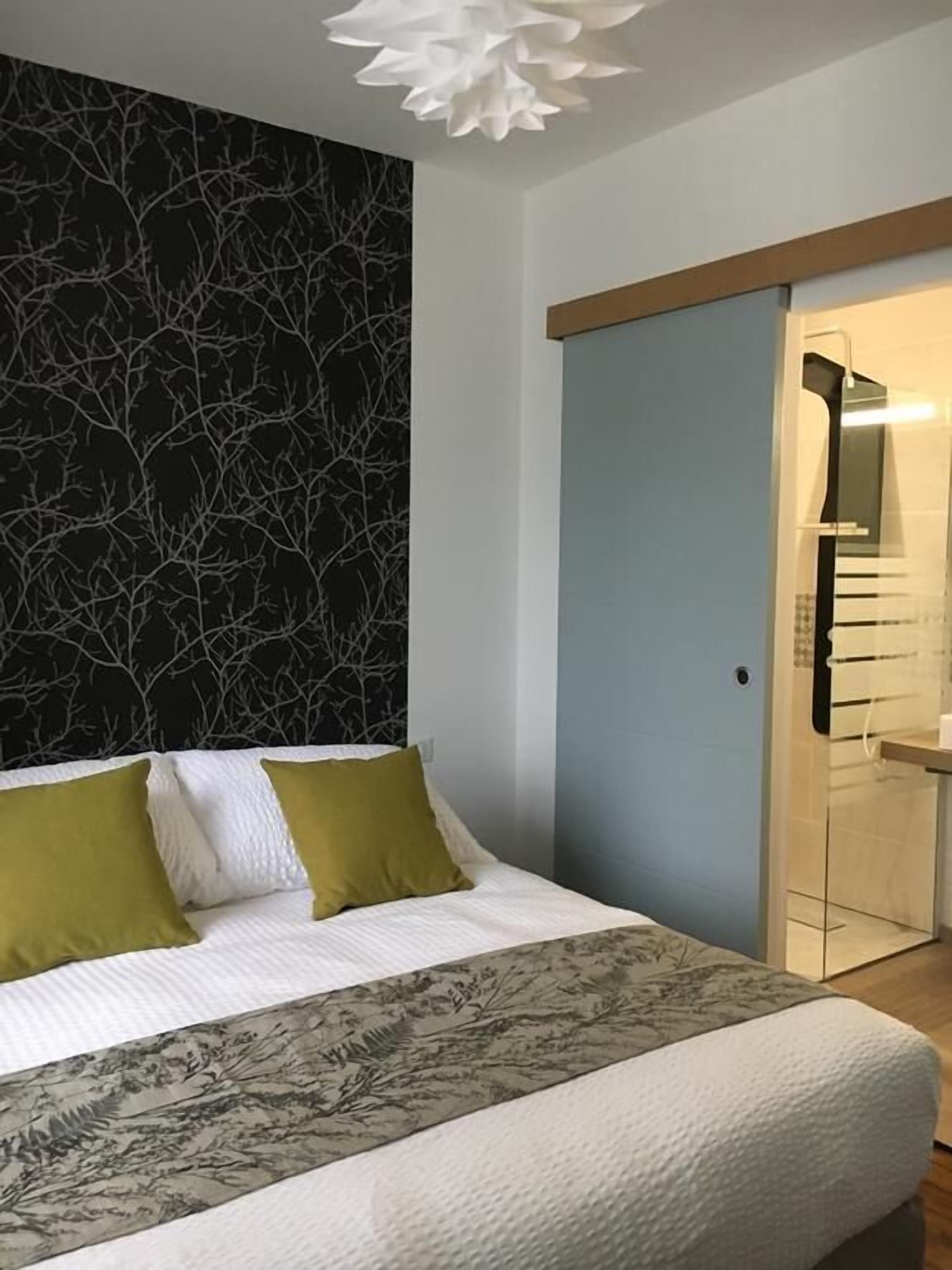A bedroom with a bed, a wall with a tree pattern, and a door leading to a bathroom.