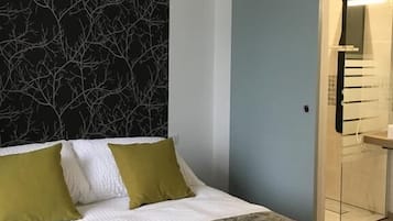 A bedroom with a bed, a wall with a tree pattern, and a door leading to a bathroom.