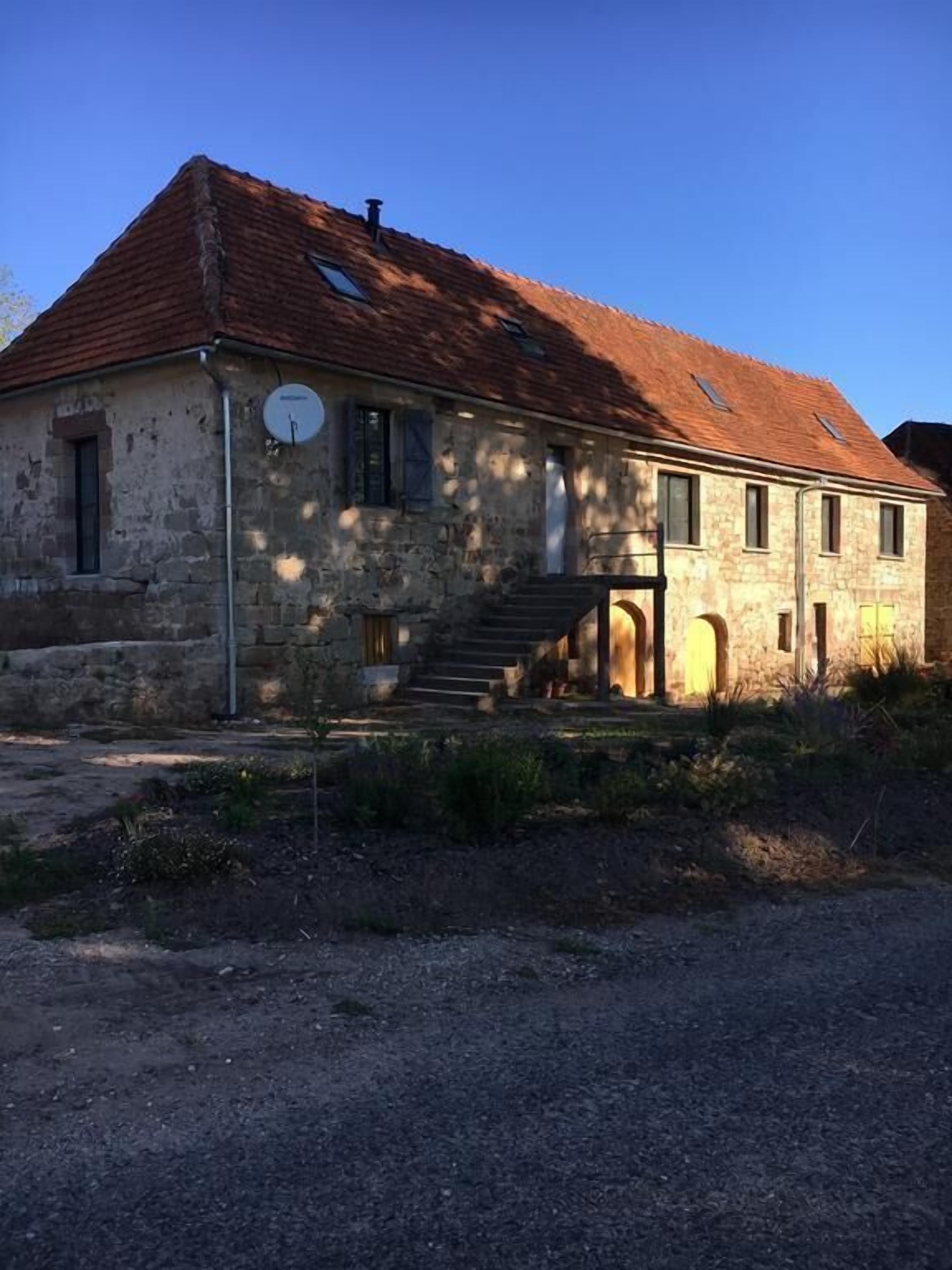 A stone building with a sloped roof, a satellite dish, and a staircase leading to a door.
