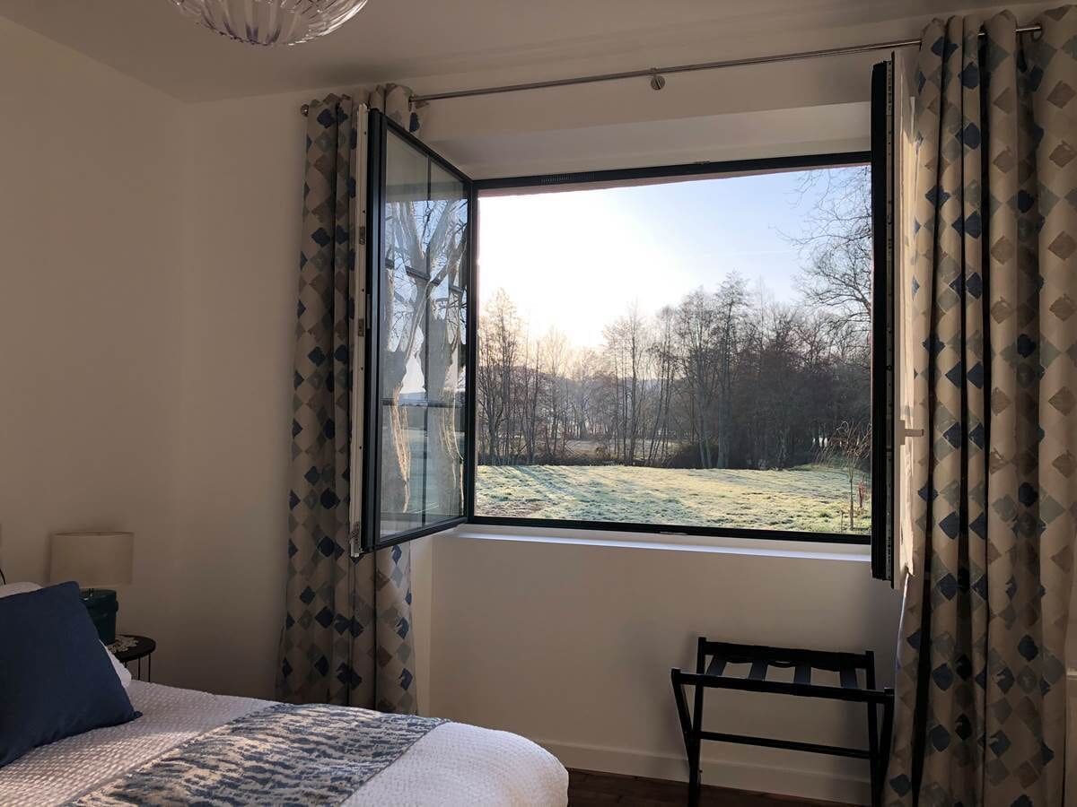 A bedroom with a large window, a bed, a chair, and a lamp.