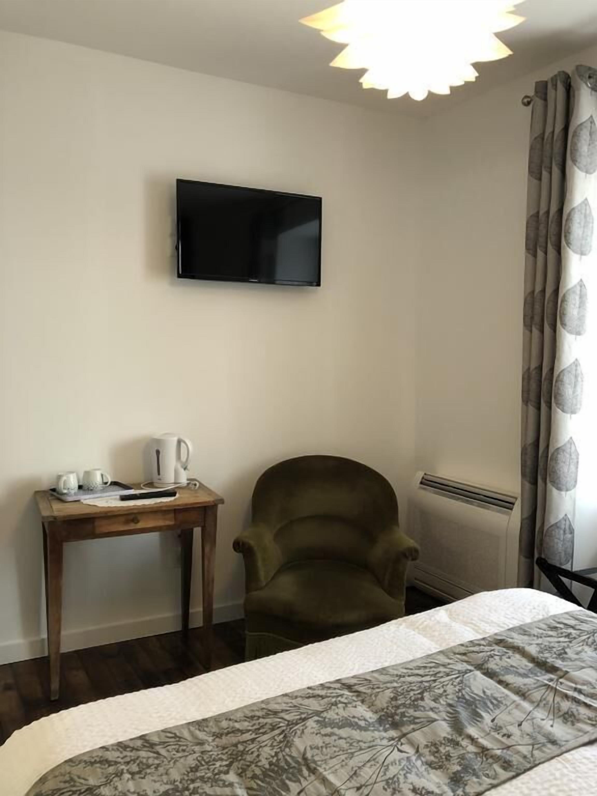 Et hotelværelse med en seng, en stol, et lille bord med elkedel og kopper, et fladskærms-TV monteret på væggen og en radiator.