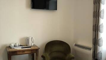 Et hotelværelse med en seng, en stol, et lille bord med elkedel og kopper, et fladskærms-TV monteret på væggen og en radiator.