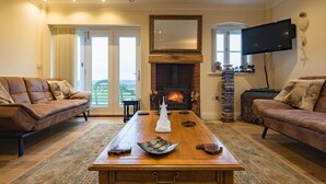 A living room with a fireplace, leather sofas, a coffee table with decorative items, and a television mounted on the wall. - The Homestead by Bloom Stays - sleeps 17 (Canterbury)