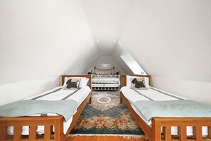 Een kamer met twee houten bedden, een bankje in het midden en een bloemenkleed.